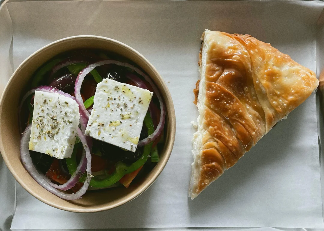 A slice of golden phyllo pie beside a Greek salad topped with feta