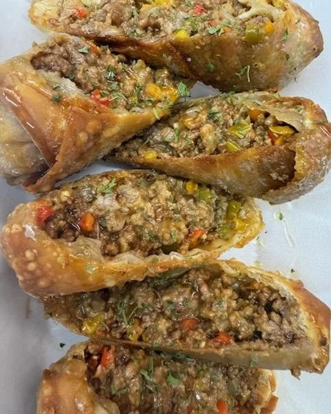 Two crispy egg rolls filled with a savory mix of meat and vegetables, garnished with herbs, served on a white plate.
