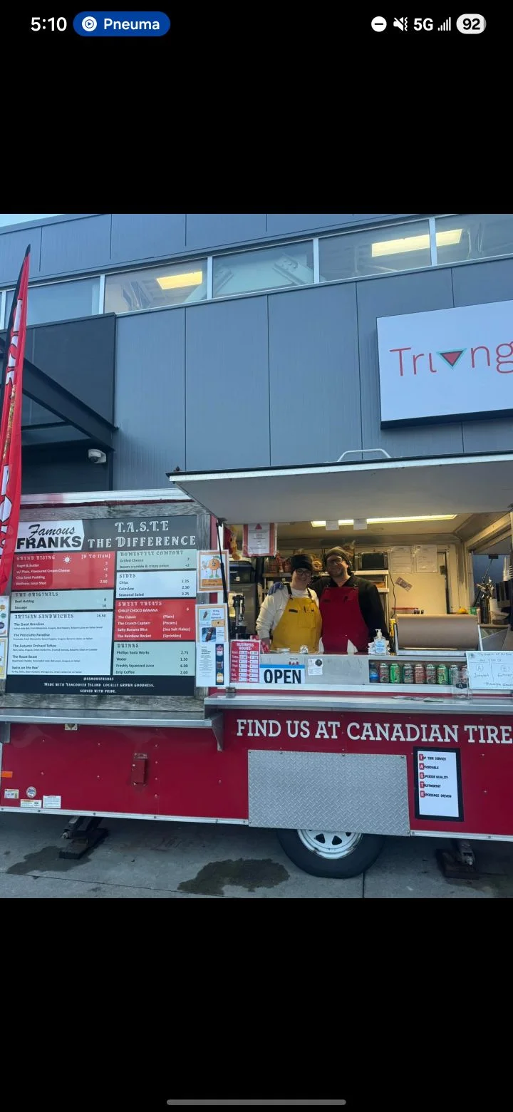 A food truck with a menu prominently displayed, featuring two vendors in front.