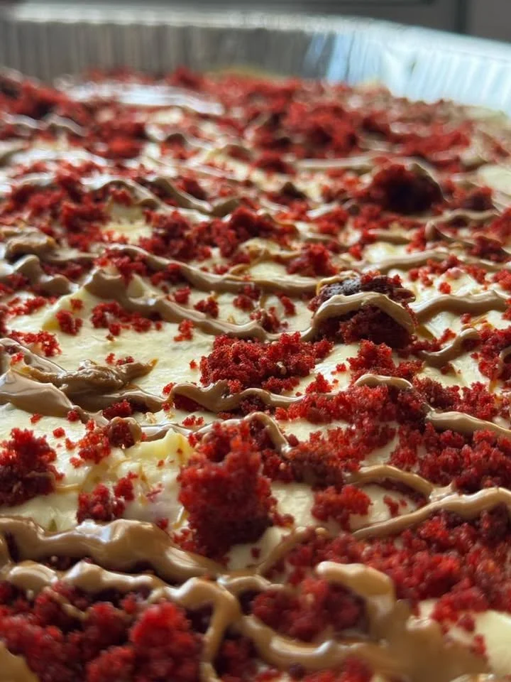 A dessert made with cream cheese frosting, red velvet crumbs, and a drizzle of chocolate on top, showing a close-up view.