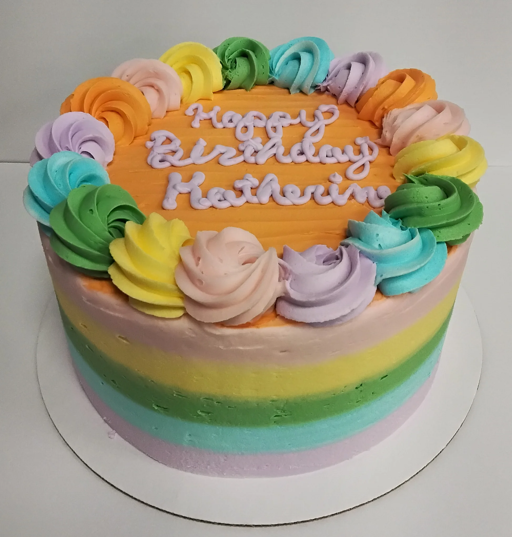 Round cake done in pastel rainbow with a swirly border on the top and says "Happy Birthday Katherine"