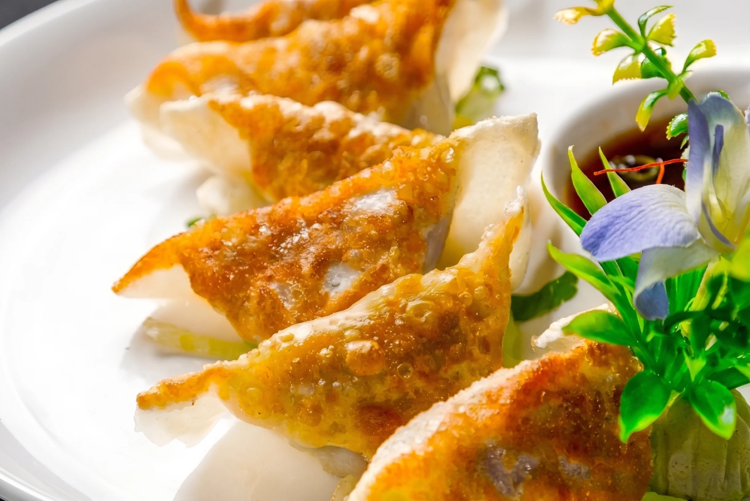 Golden-brown dumplings served with dipping sauce and garnished with flowers.