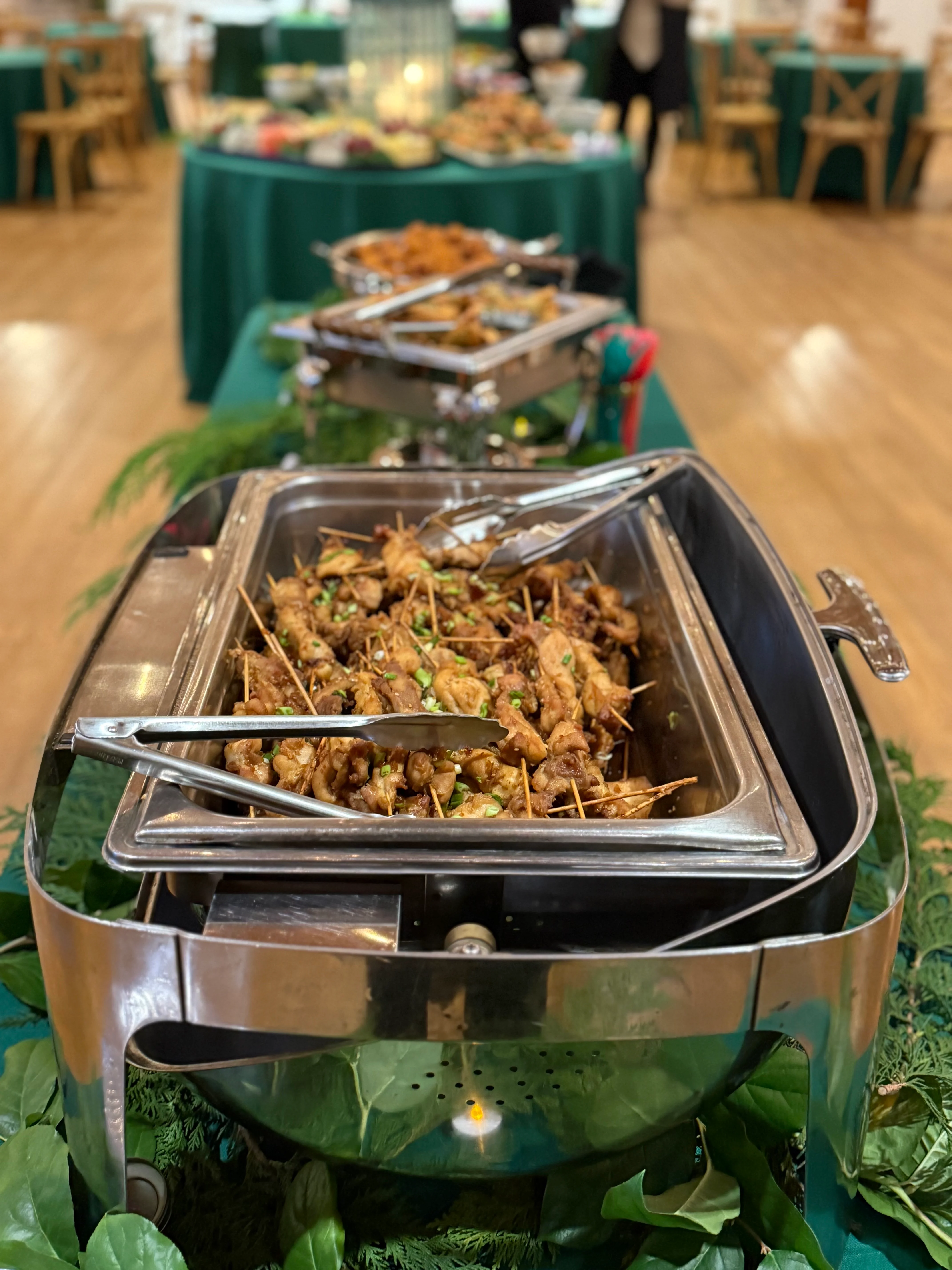 Catering chafing dish set on a decorated table and filled with skewers.