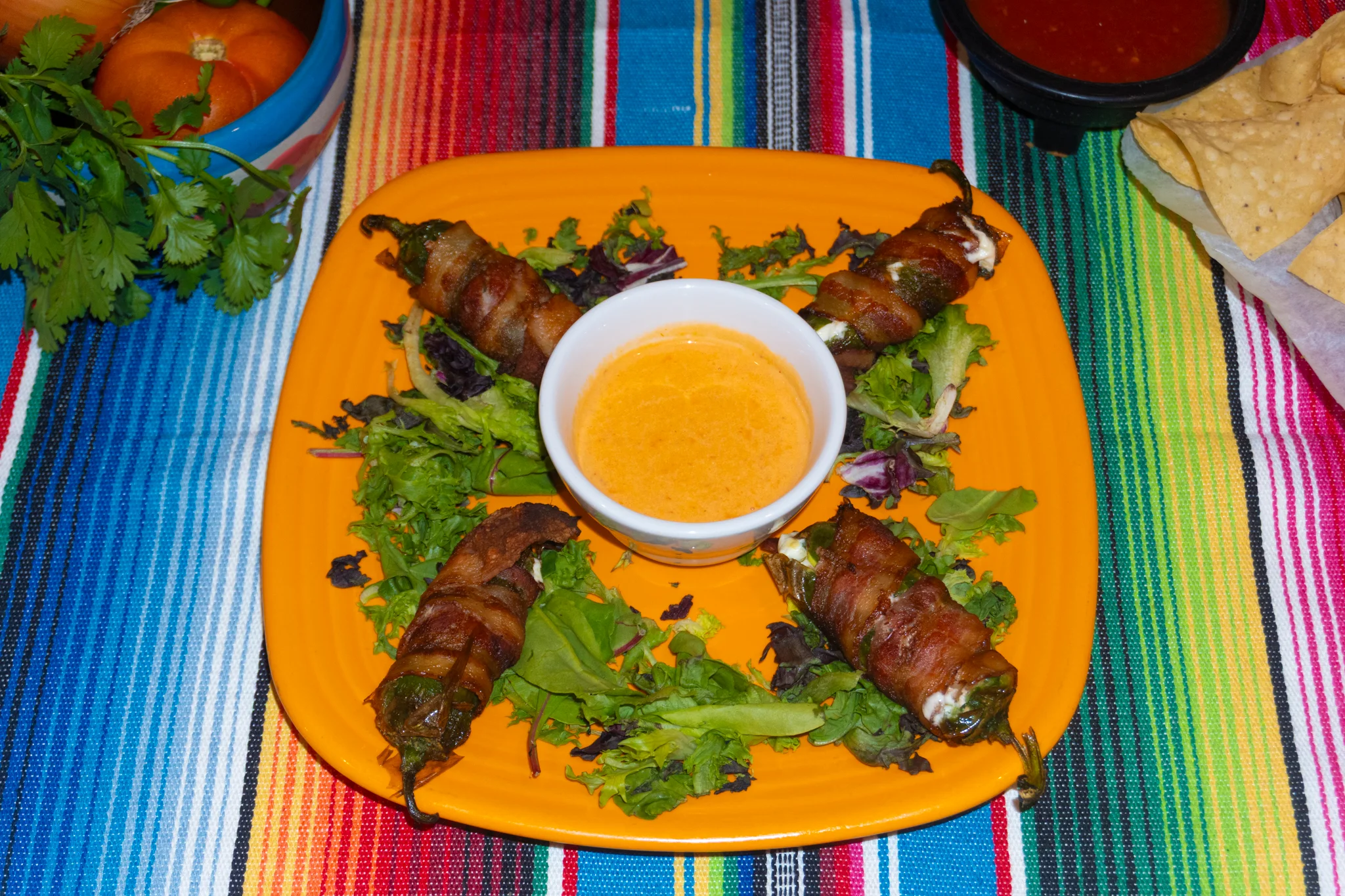 Bacon-wrapped jalapeño poppers served with dipping sauce on a vibrant plate