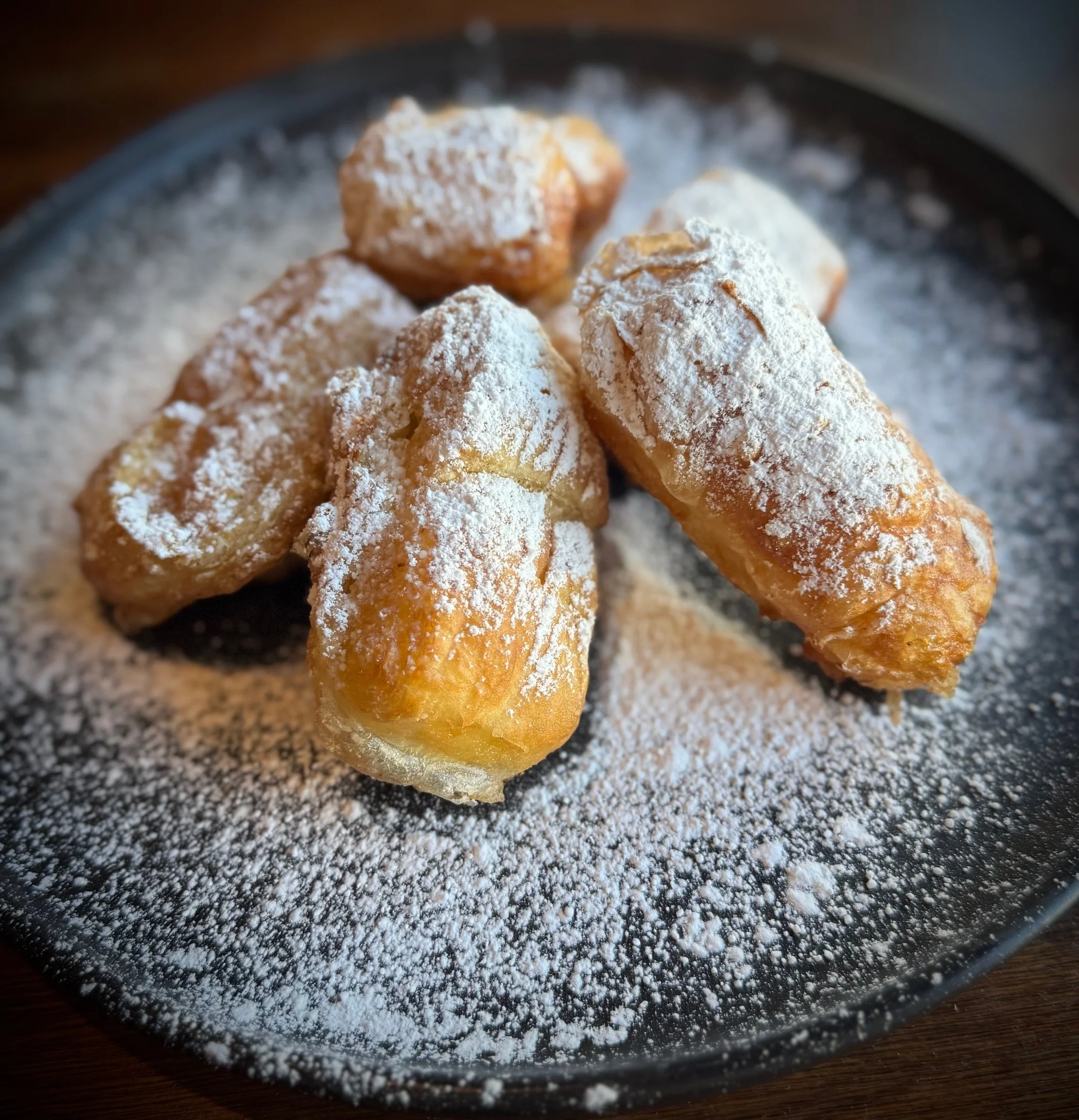 Delicious beignets dusted with powdered sugar on a black plate