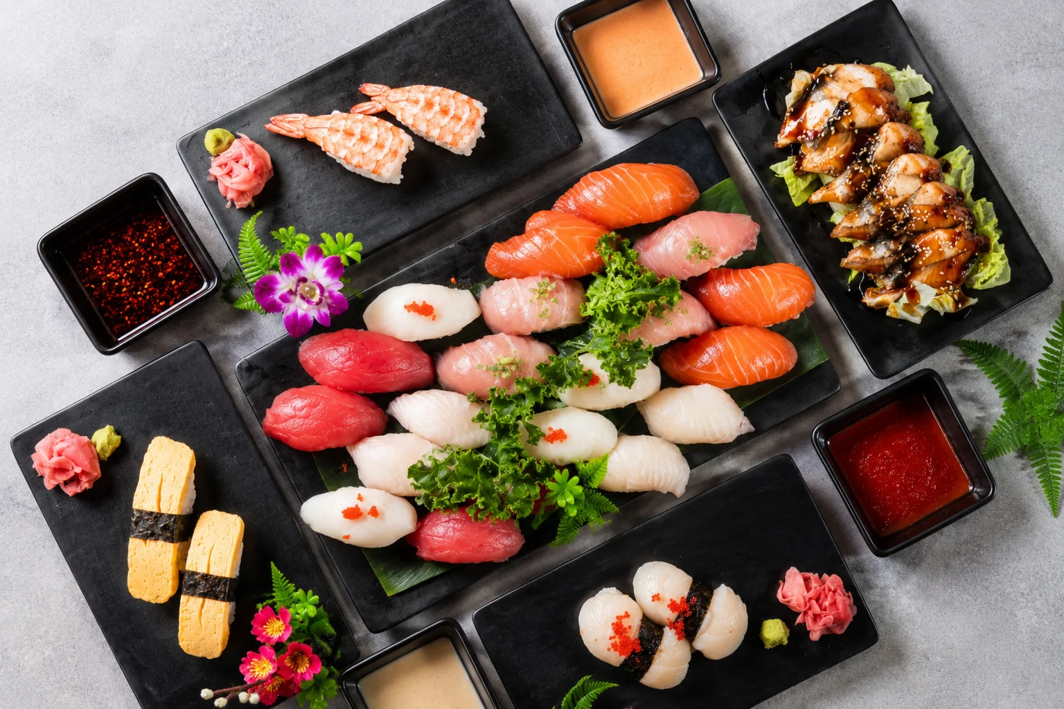 Colorful sushi rolls on a black plate with wasabi and ginger.