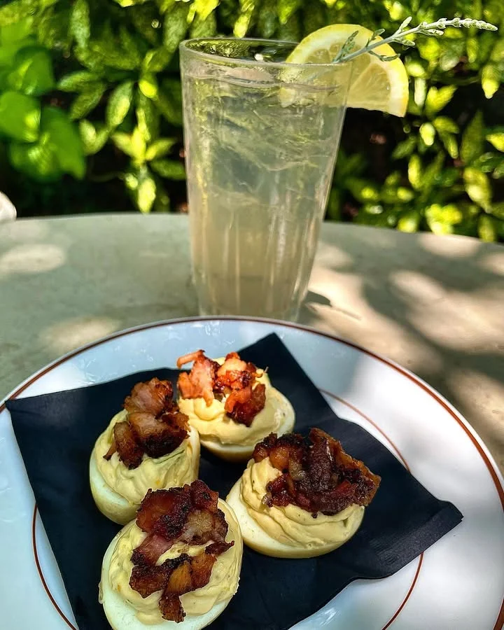 A plate of savory treats topped with crispy bacon, accompanied by a tall glass of fizzy lemonade garnished with lemon.