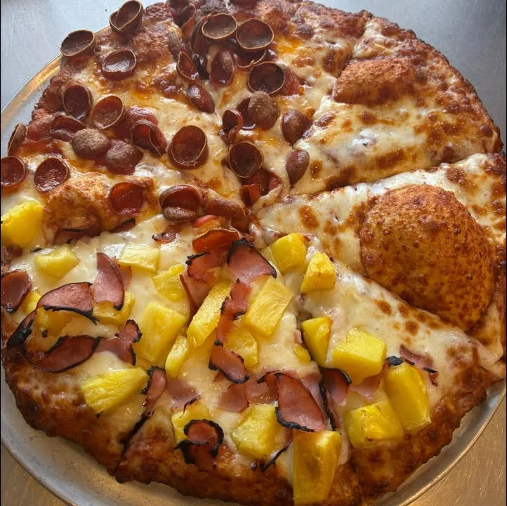 A large pizza divided into two halves. One half features pepperoni, while the other is topped with ham and pineapple.