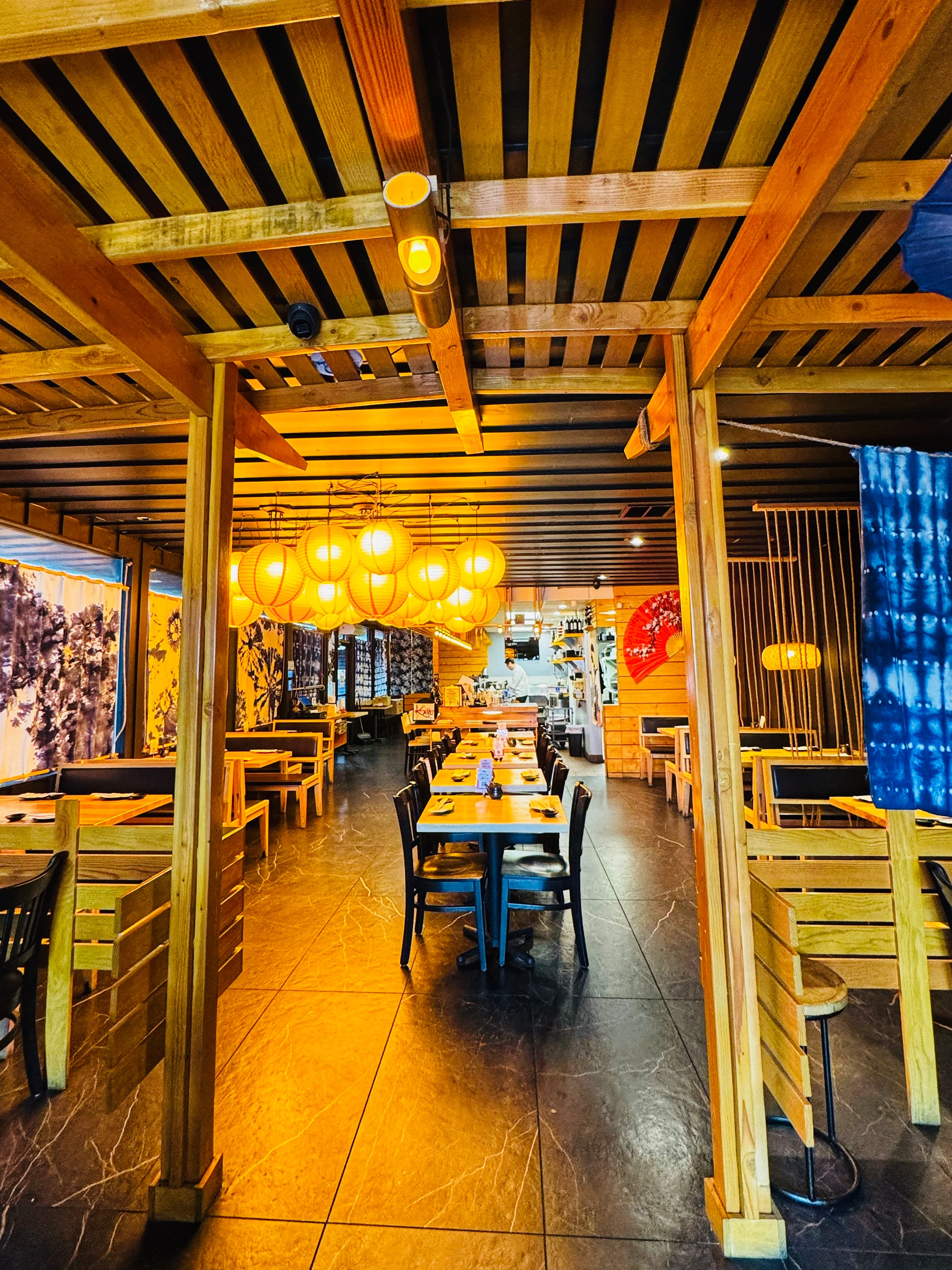 An inviting dining area with wooden decor, featuring tables and chairs, bright hanging lights, and colorful lanterns.