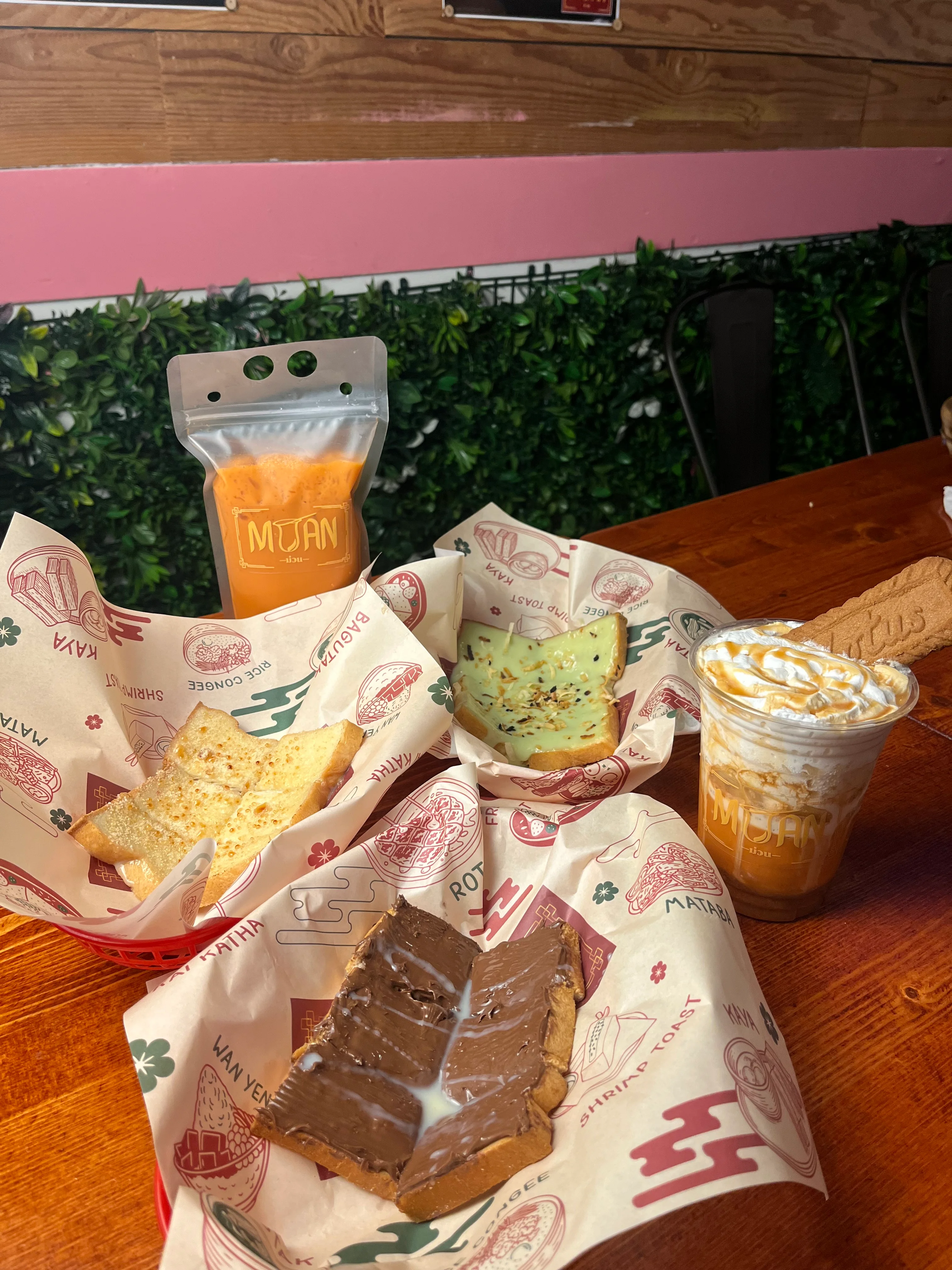 An assortment of toasted bread with various toppings and an iced beverage served in a plastic cup on a wooden table.