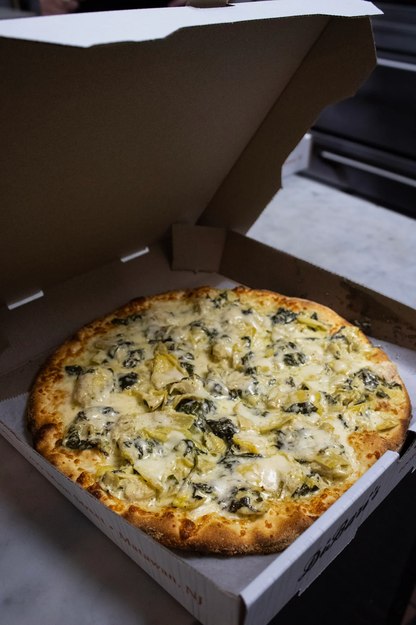 Creamy spinach artichoke pizza in a takeout box