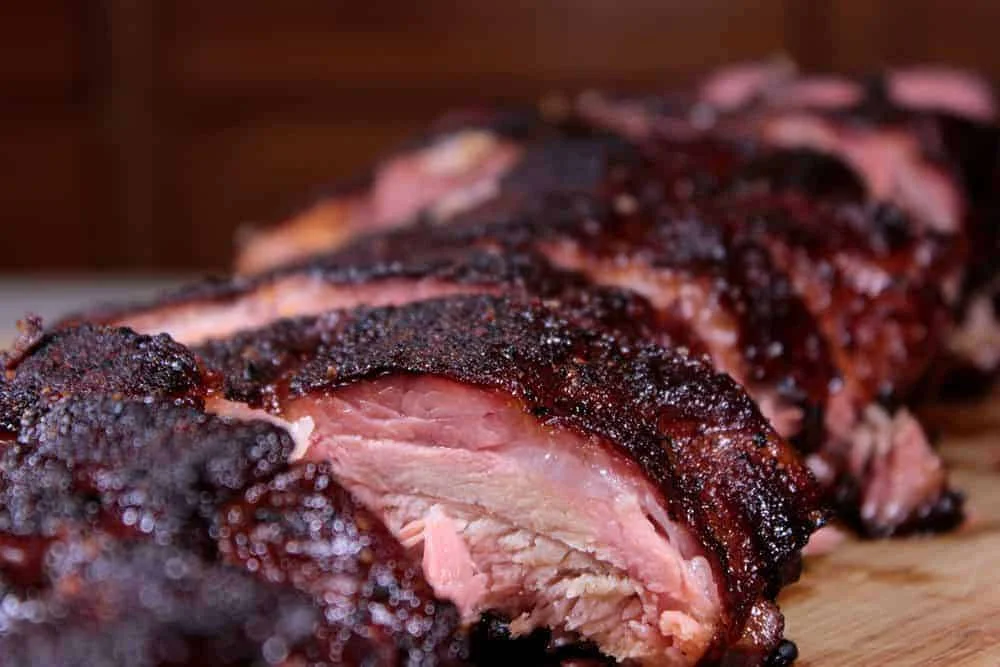 Close-up of a beautifully smoked and sliced piece of meat, showcasing a dark, crispy exterior and juicy interior.