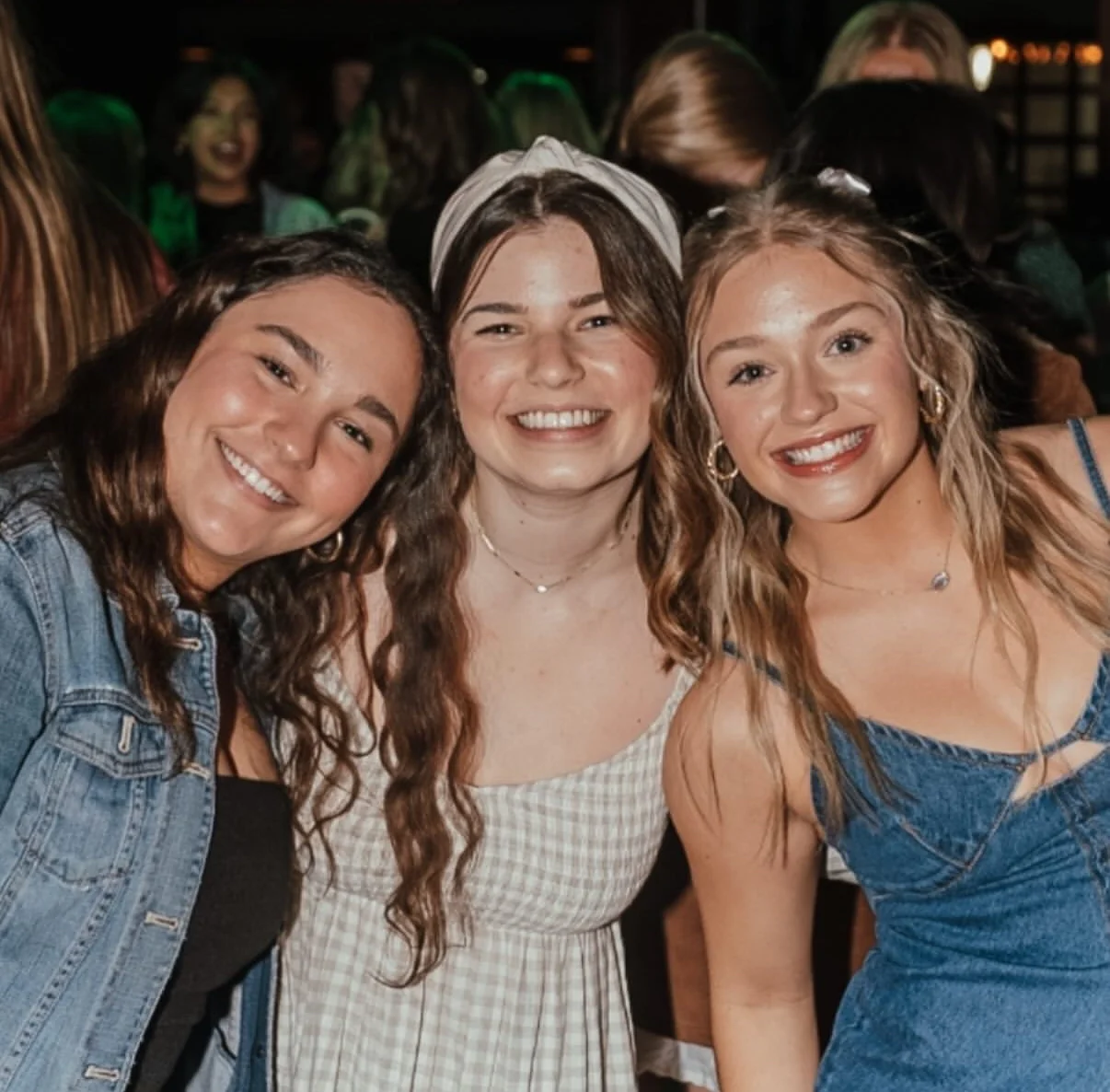 Three friends smiling together at a lively event
