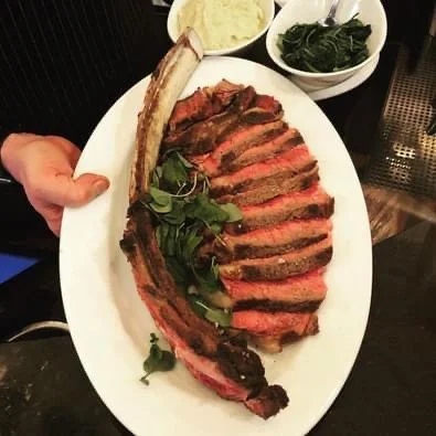 Cooked steak sliced into several pieces with salad in the middle of the plate and two small bowls in the upper right hand corner of the image with mashed potatoes in one and spinach in the other 