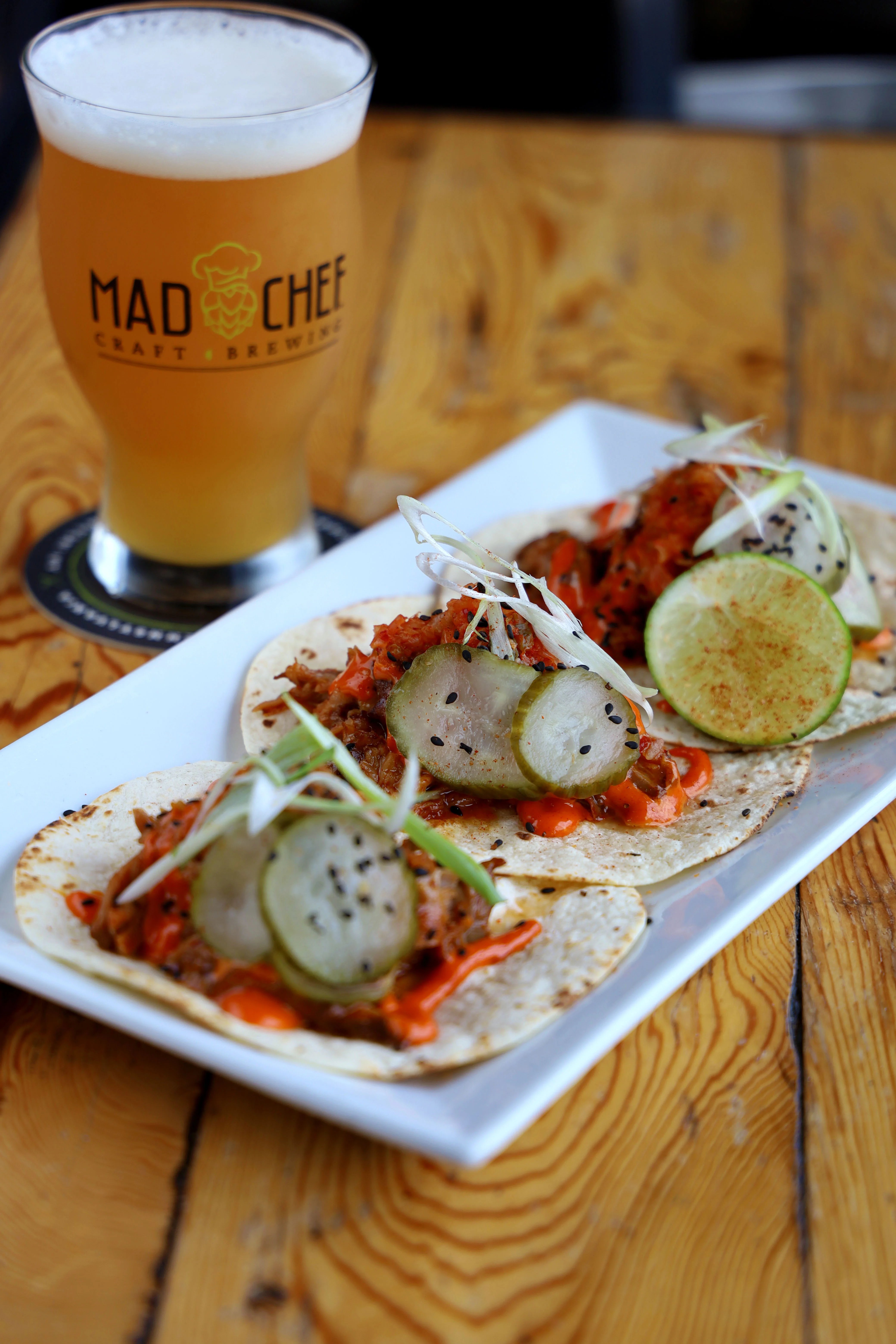 Three tacos with pulled meat, pineapple, and lime on a plate.