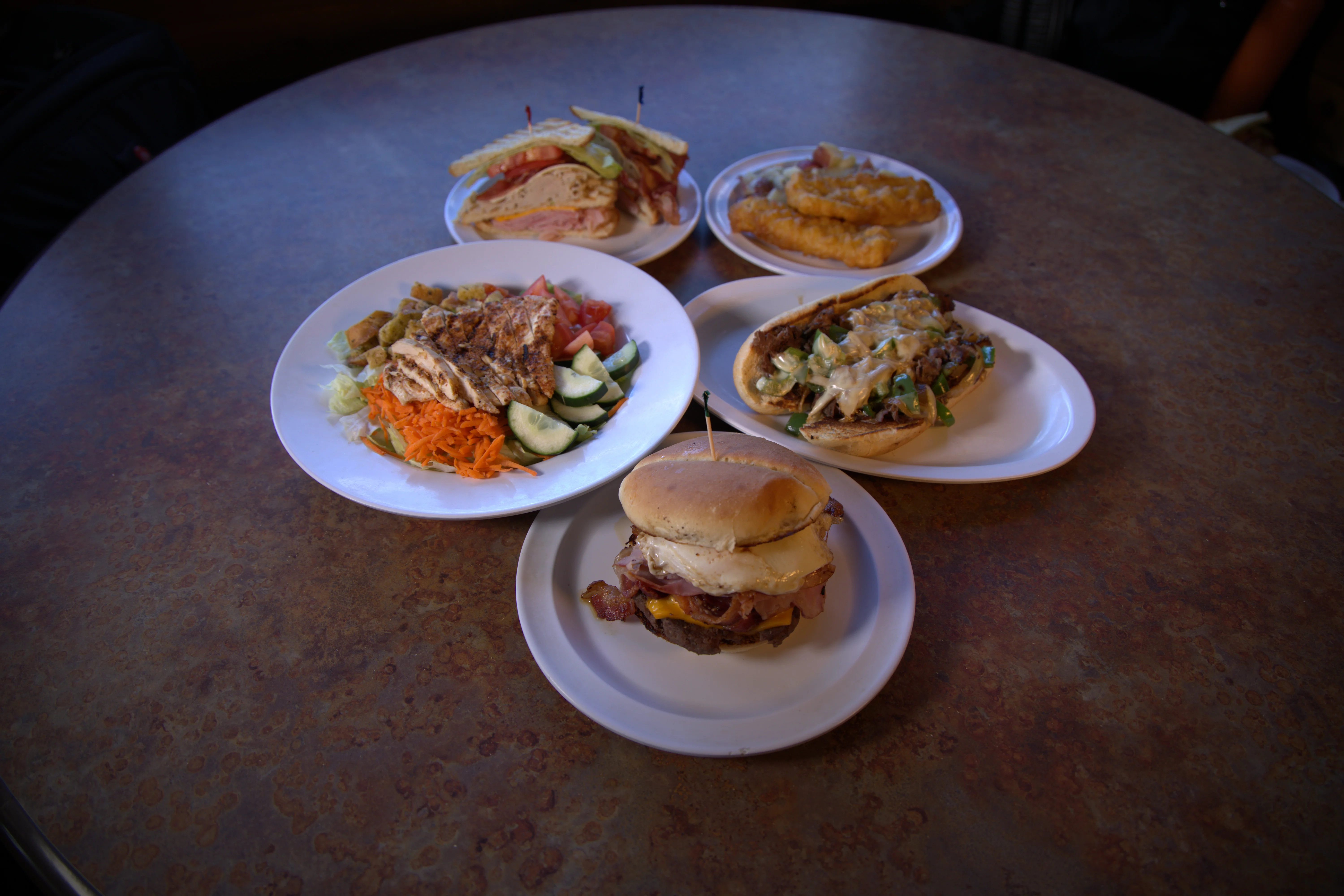 A variety of dishes presented on white plates, including a sandwich, salad, and a meat-filled roll, all arranged on a round table.