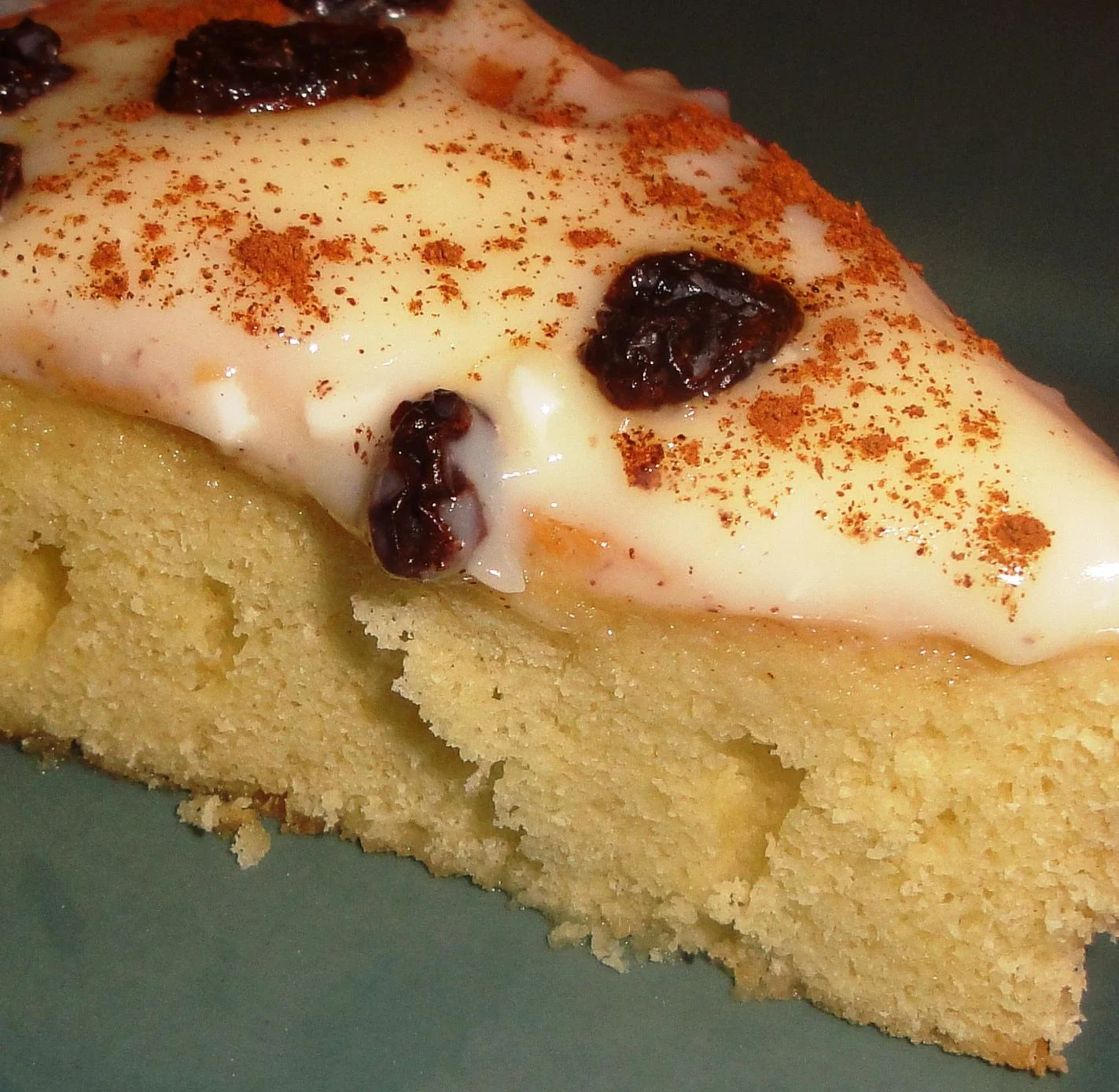 A piece of cake with a creamy icing and a sprinkle of cinnamon, topped with dried fruit.