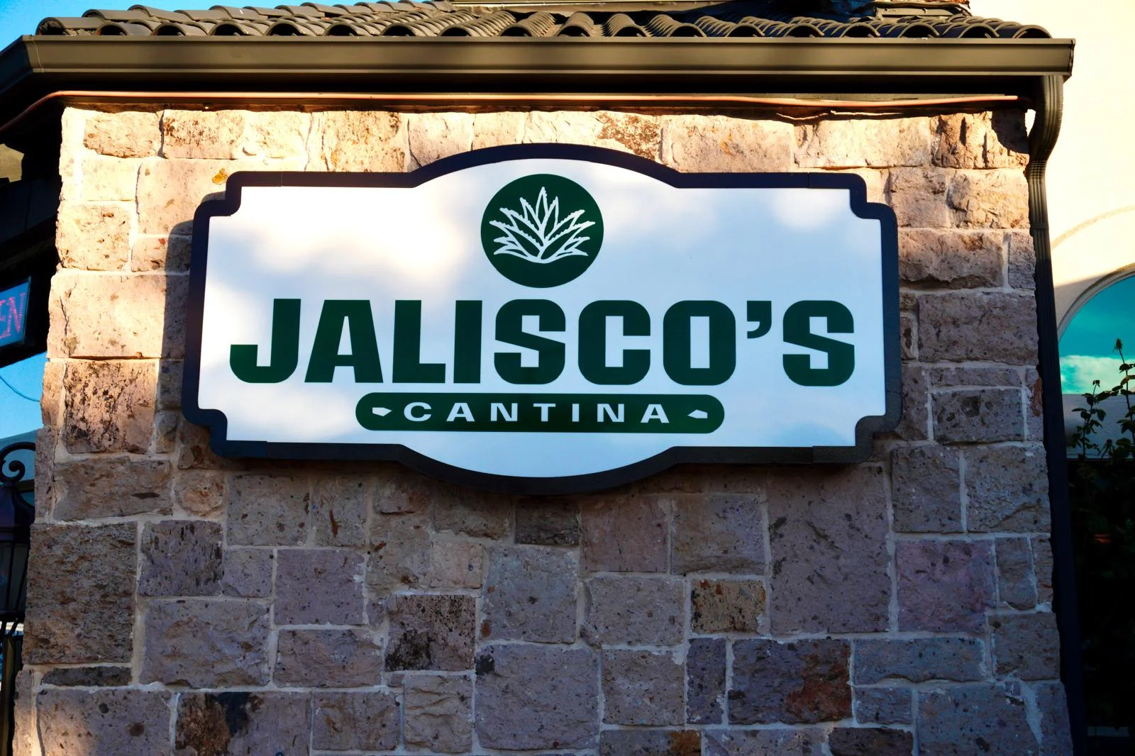 The exterior view of a restaurant named Jalisco's Cantina, showcasing a stone facade and a classic red vehicle parked nearby.