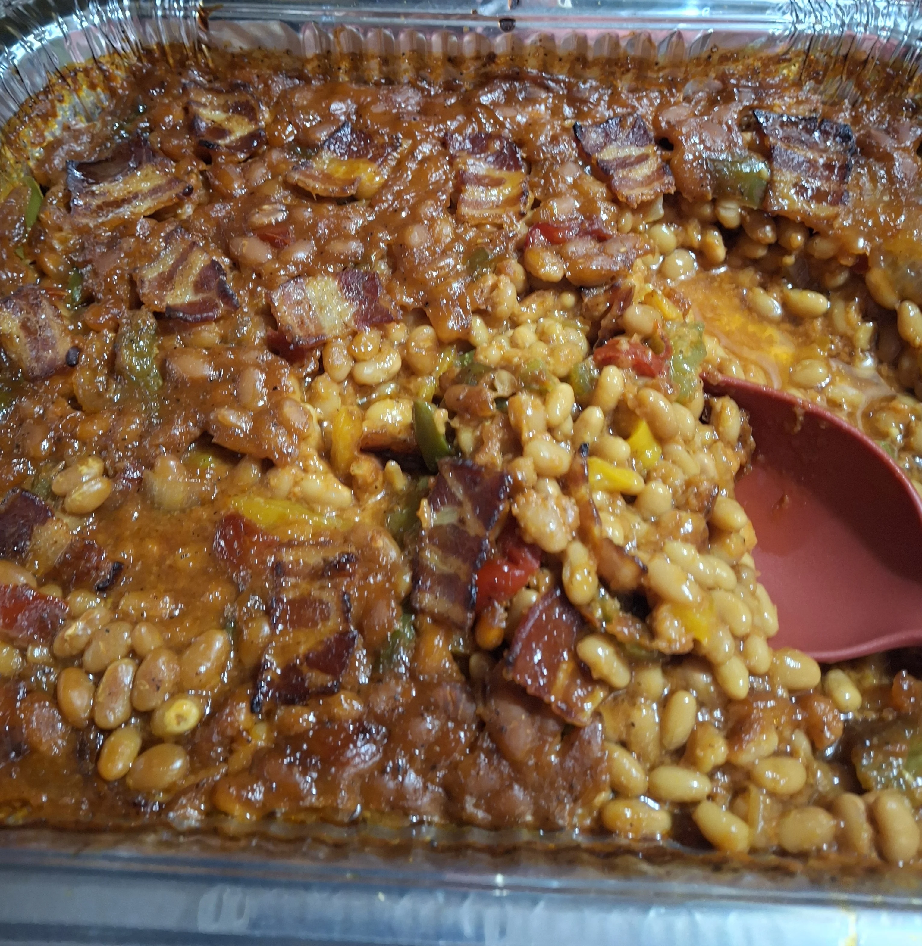 A baking dish filled with a mixture of baked beans, bacon, and vegetables, topped with a rich sauce.