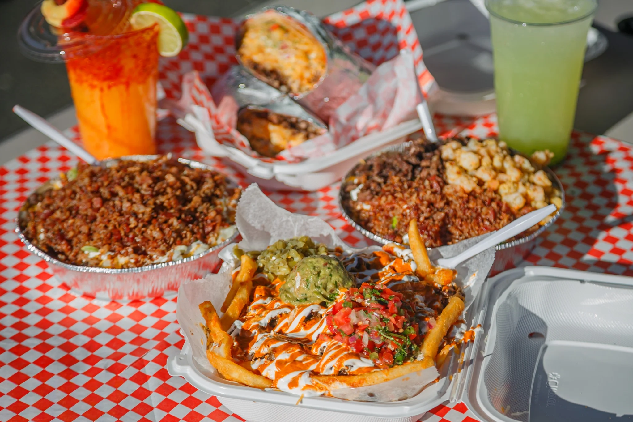 A spread of delicious Mexican-style dishes including loaded fries with toppings, tacos, and refreshing beverages on a picnic table.