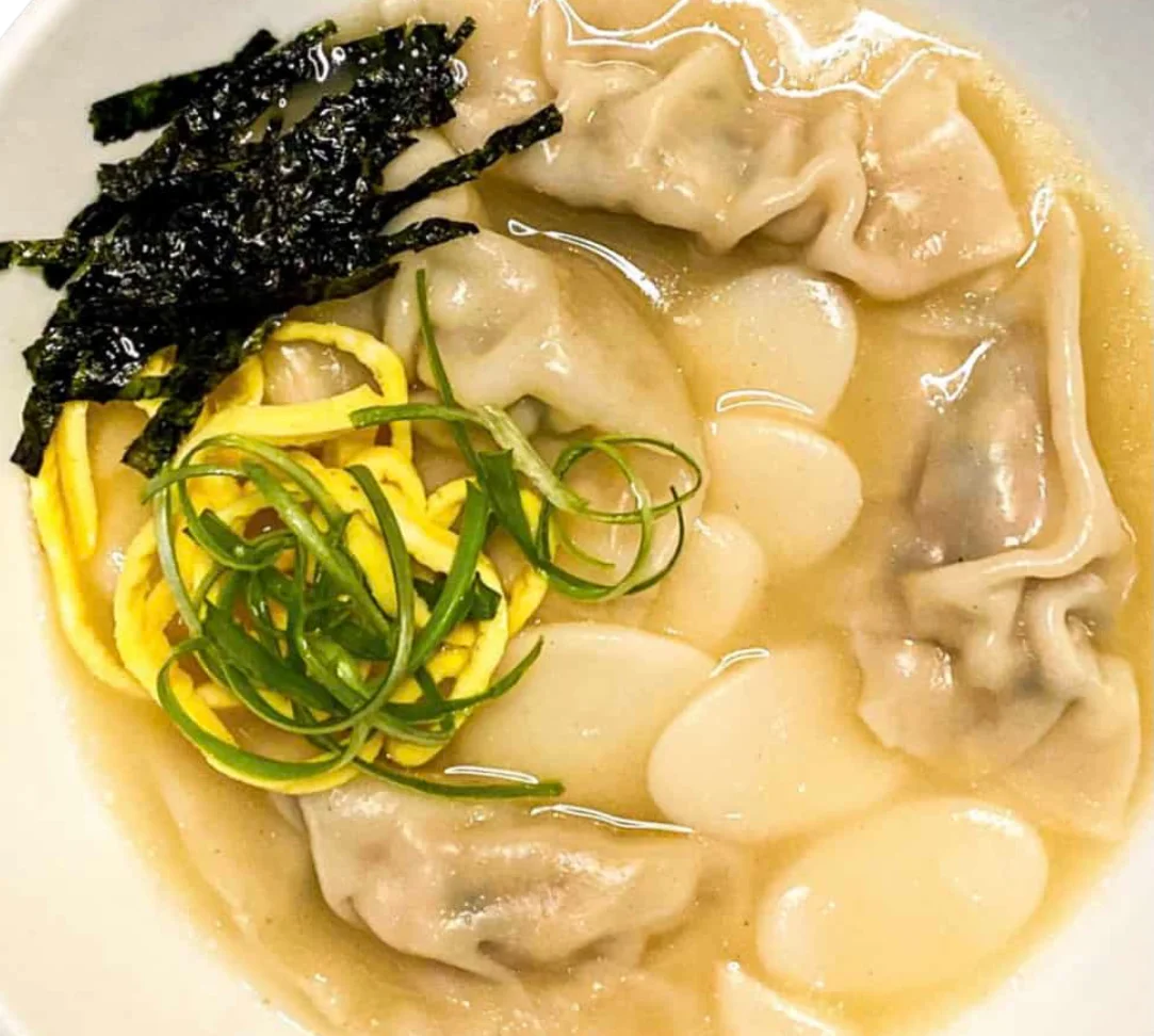 Bowl of dumpling soup with green onions, egg strips, and seaweed.
