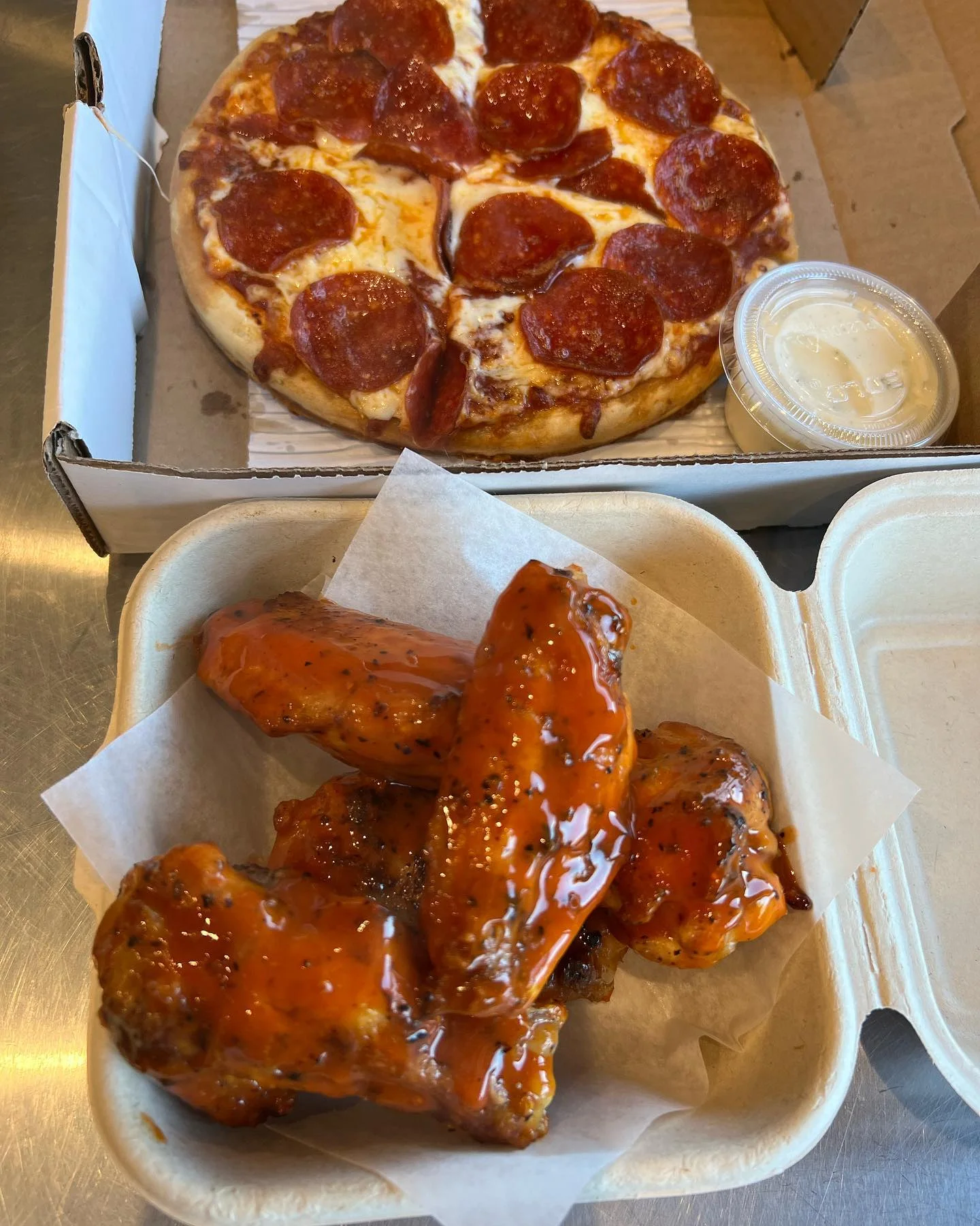 A meal consisting of a pepperoni pizza and a serving of spicy chicken wings with a side of dipping sauce.
