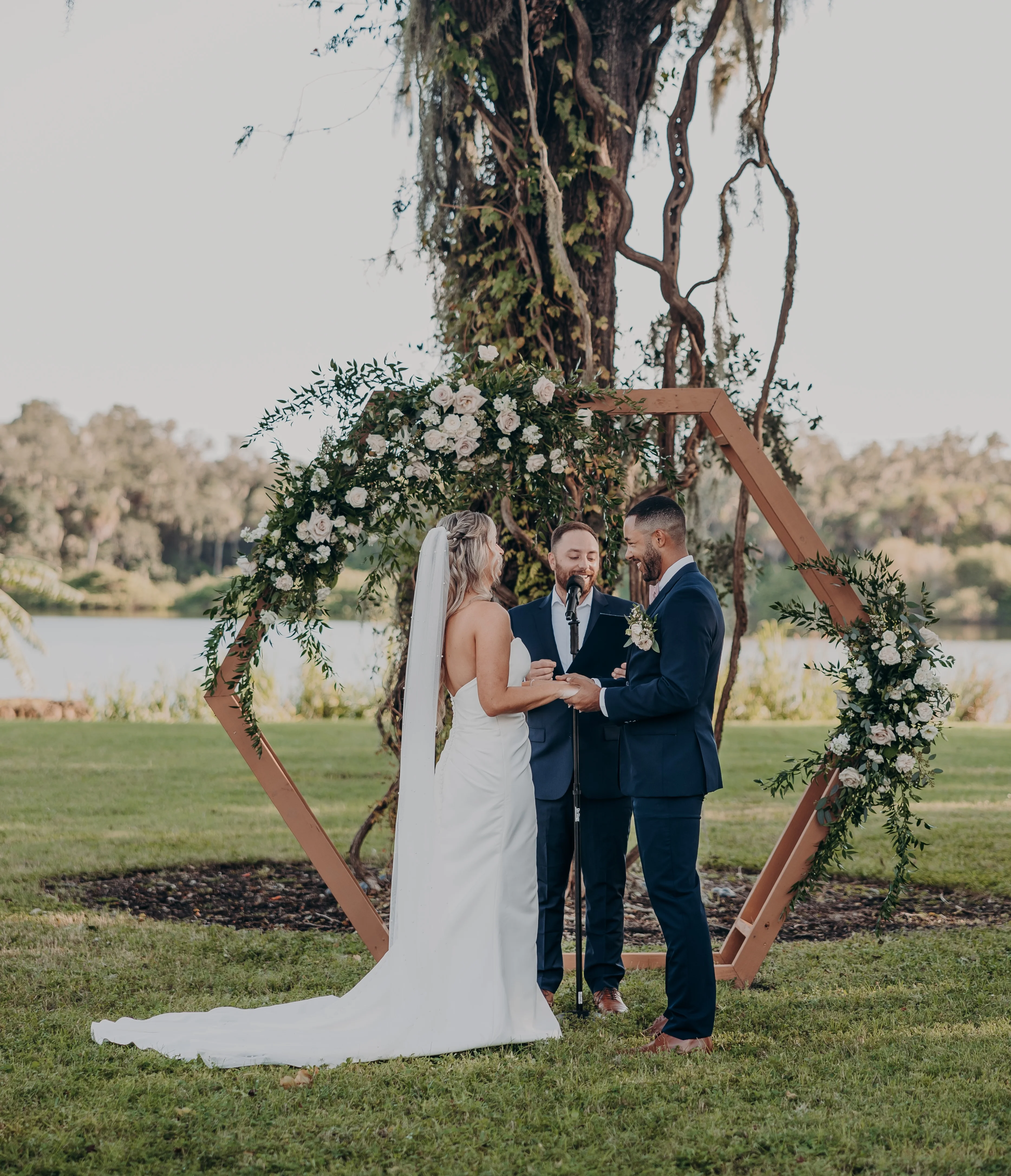 Outdoor wedding ceremony by a lake with floral arch