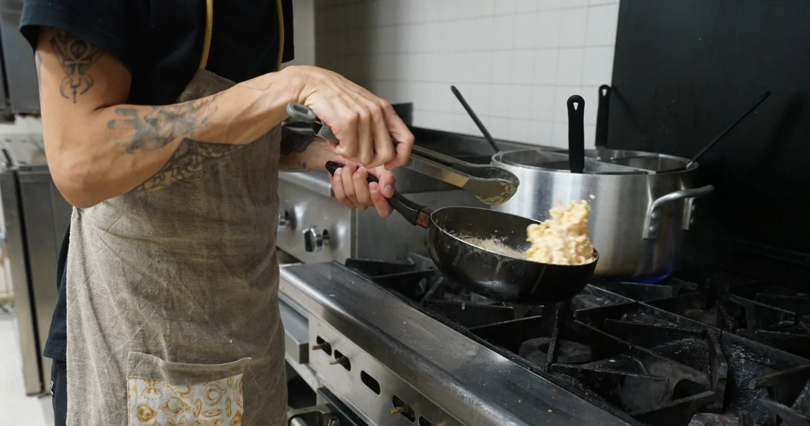 Chef sautéing pasta in a busy restaurant kitchen