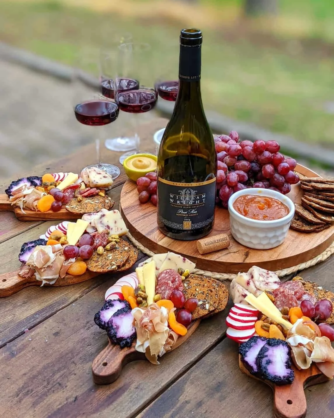 A beautifully arranged platter featuring assorted cheeses, meats, fruits, and crackers, accompanied by a bottle of wine and glasses filled with red wine.