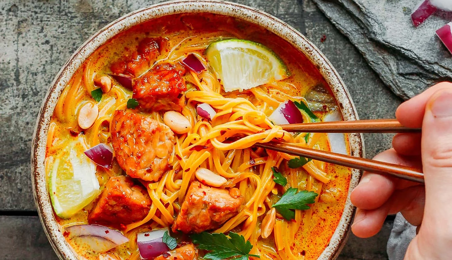 Bowl of Thai curry noodles with chicken and lime