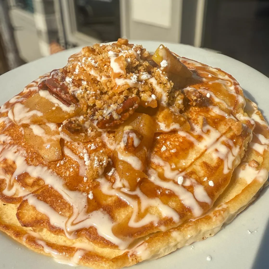 Another view of a stack of pancakes topped with caramelized apples, crumbly topping, and a drizzle of icing.