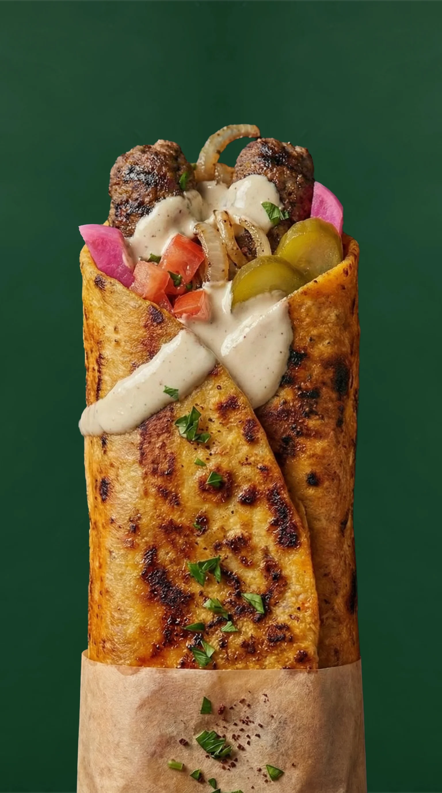 A delicious wrap filled with grilled meat, topped with onions, tomatoes, pickles, and a creamy sauce, all wrapped in a toasted tortilla.