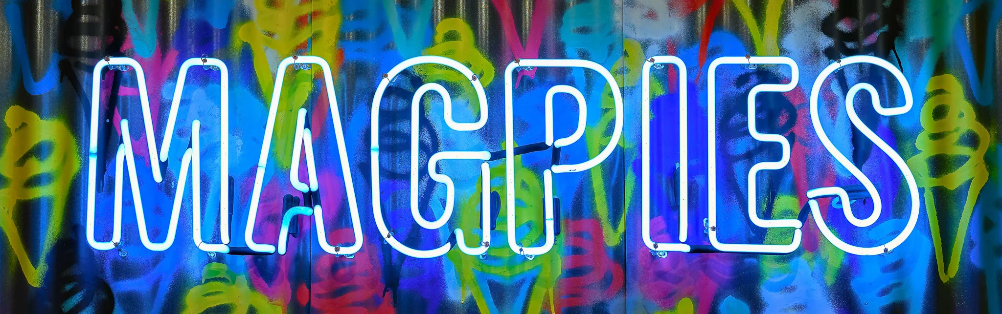 Neon sign reading 'MAGPIES' against a colorful graffiti background
