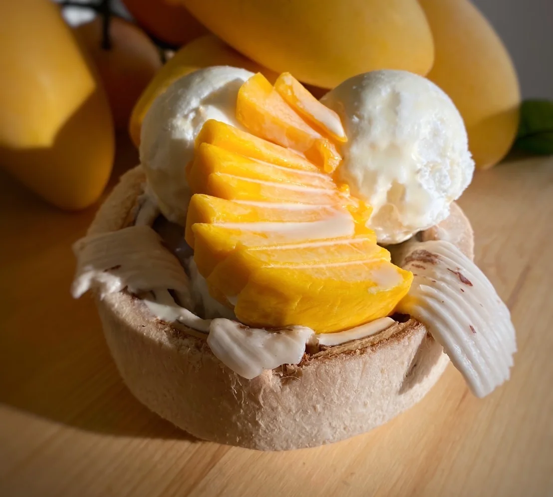Delicious coconut bowl with mango and ice cream, surrounded by fresh mangoes.