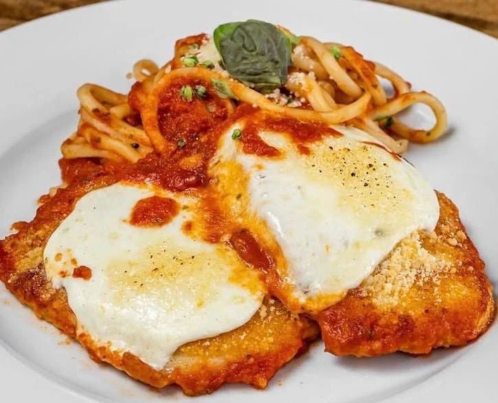 A plate featuring fried chicken topped with marinara sauce and melted mozzarella, served alongside pasta.