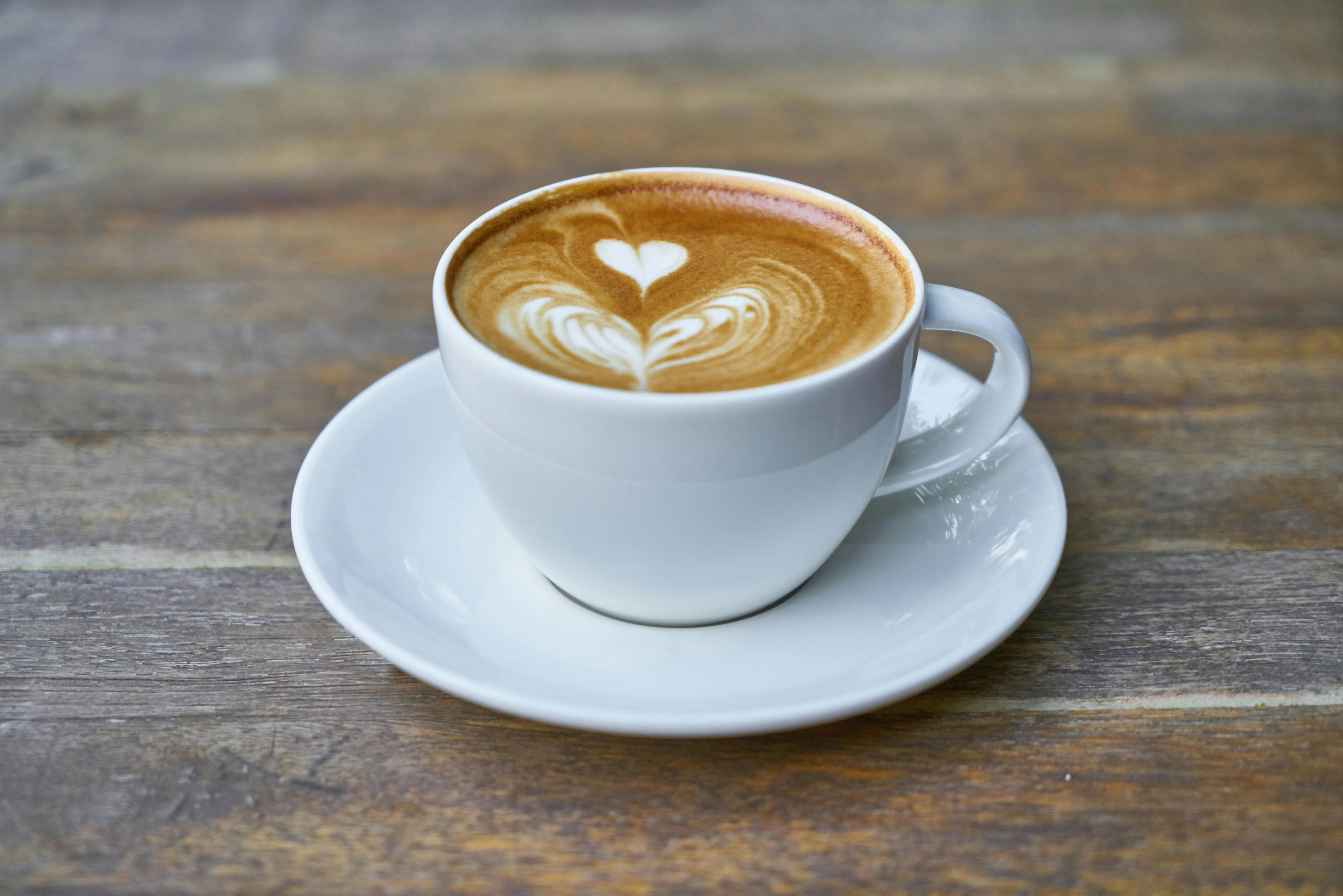 Latte art heart in a white cup on a wooden table