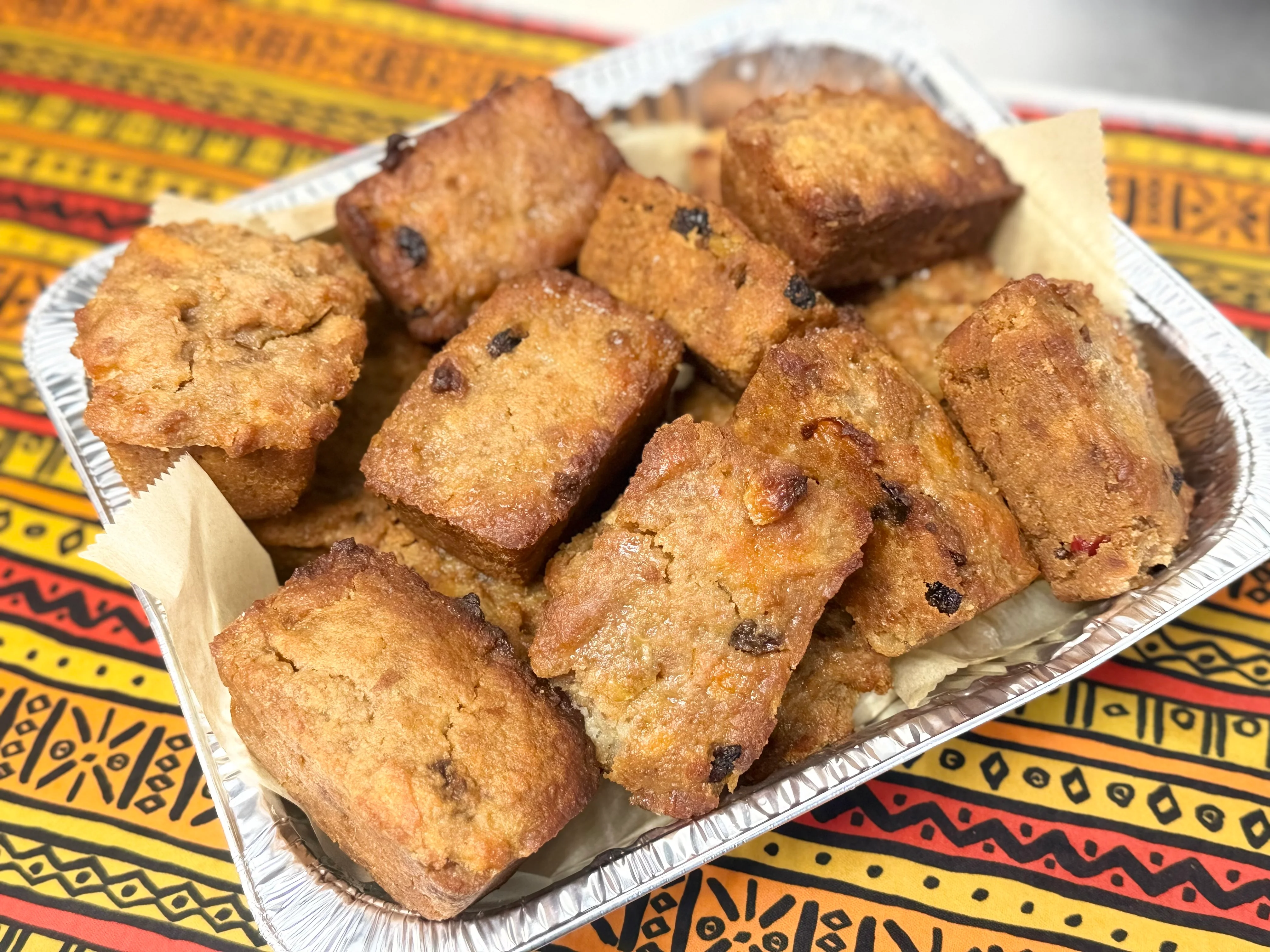 A basket of crunchy bite-sized snack pieces lined with parchment paper, set on a colorful tablecloth.