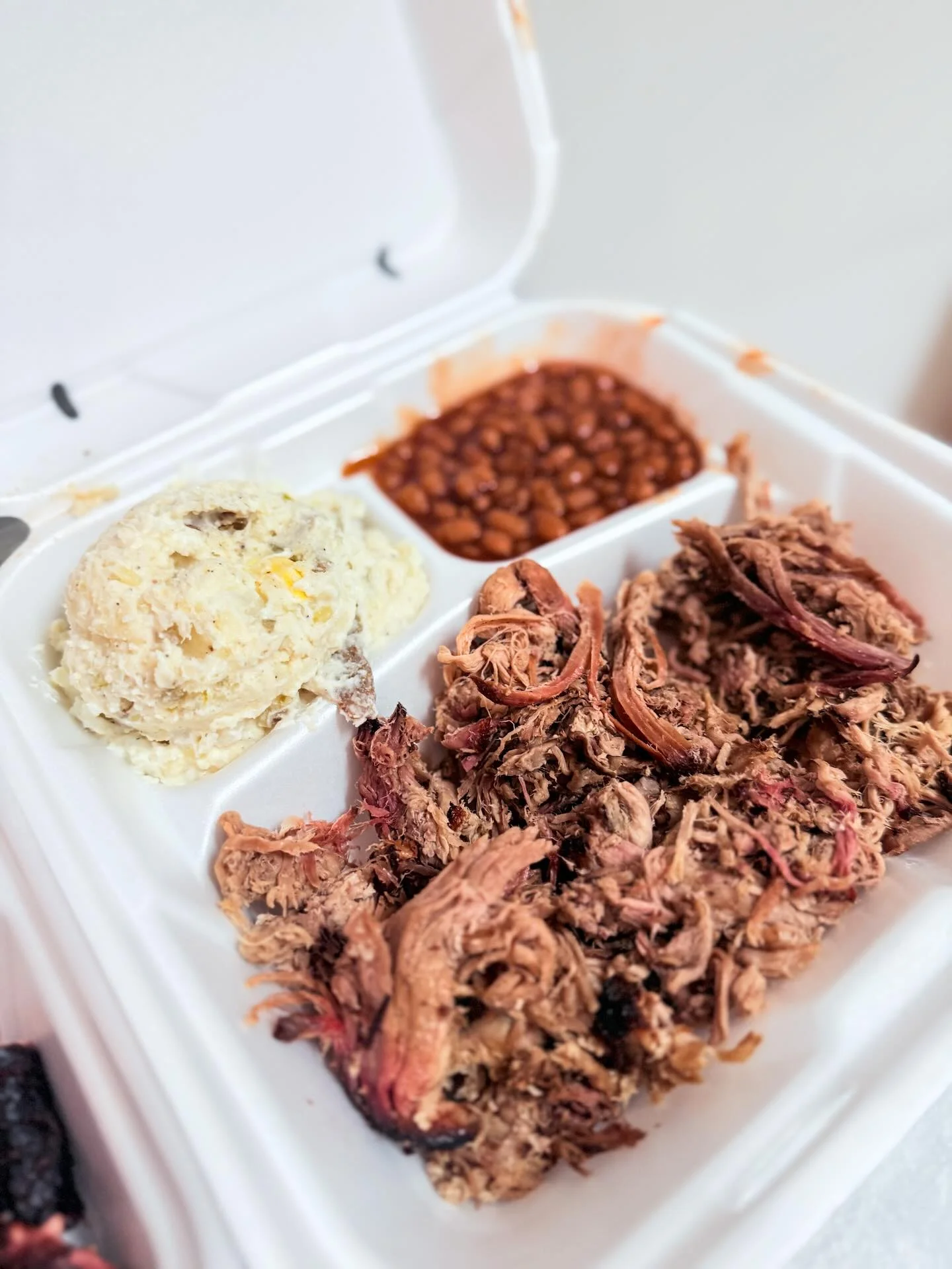 A takeout container with pulled pork, coleslaw, and baked beans neatly divided into sections.