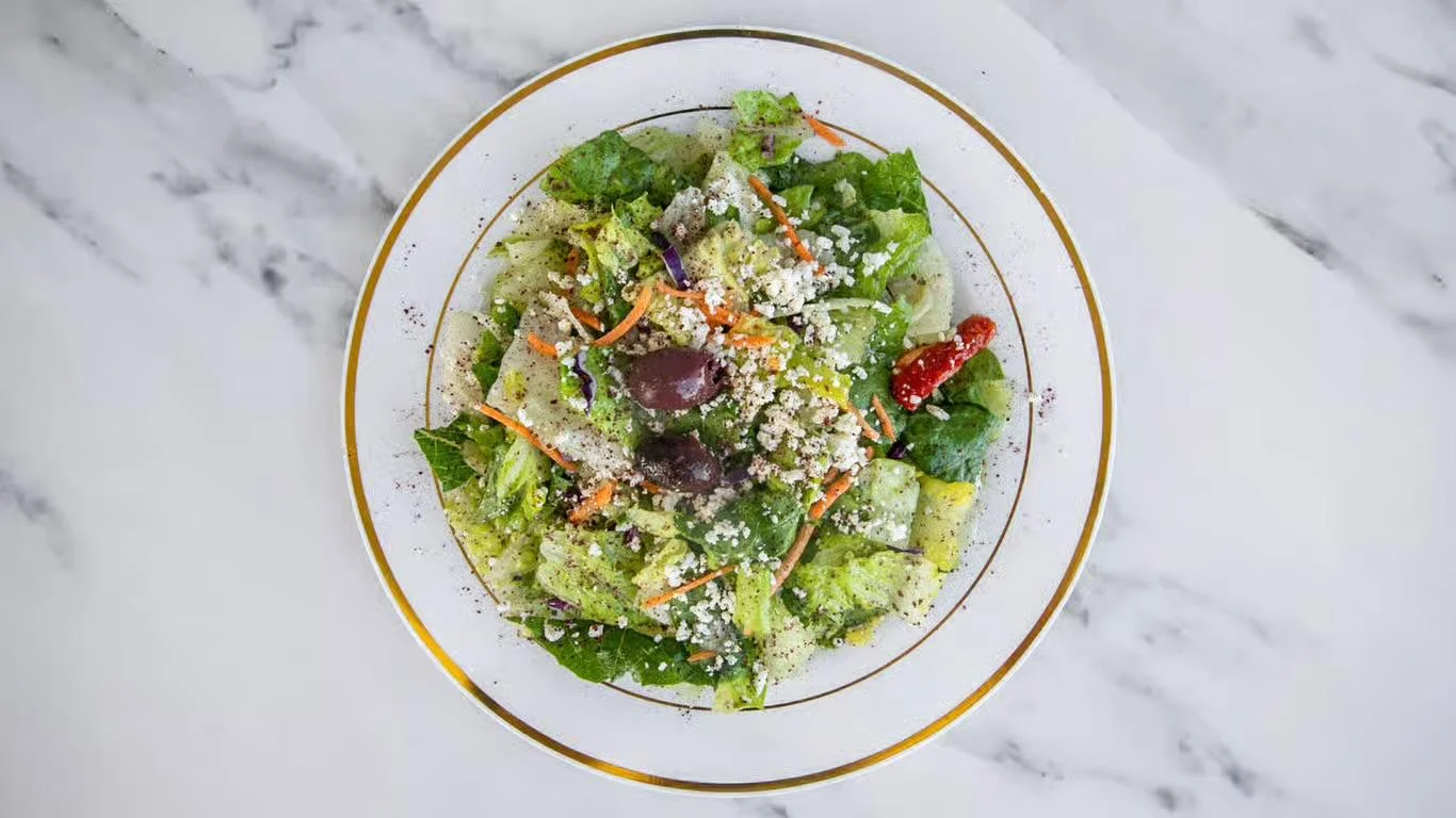 A colorful salad made with fresh greens, carrots, olives, and topped with crumbled cheese.