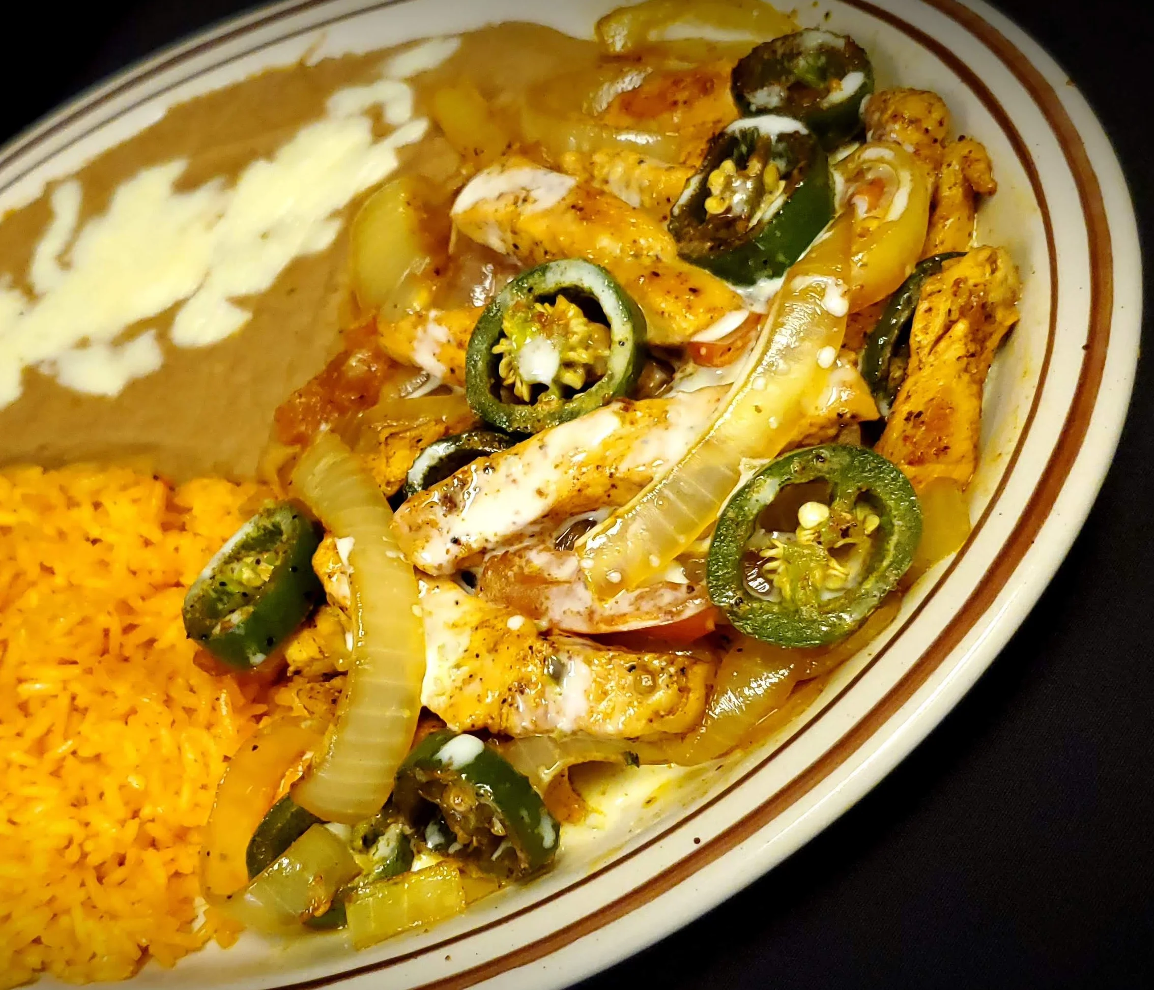 Plate of Mexican Azada from El Charro Mexican Grill, featuring tender grilled chicken with sautéed onions, tomatoes, and jalapeños, topped with creamy queso dip, served with a side of Mexican rice and refried beans.