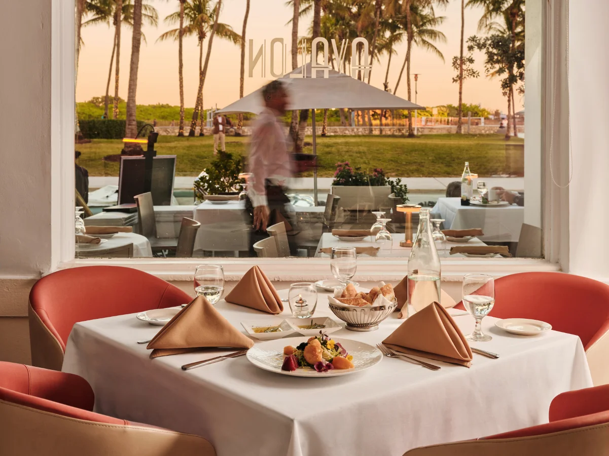 A vibrant Art Deco building with palm trees and an American flag, featuring an outdoor dining area.