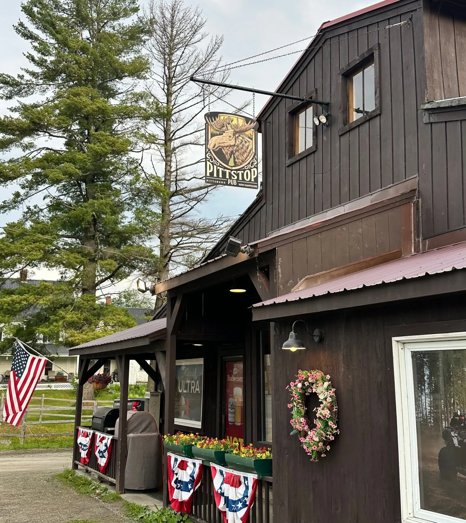 A cozy pub exterior illuminated at night, surrounded by snow. The building features a sign and an American flag.