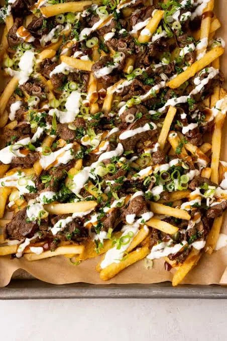 A generous serving of loaded fries topped with seasoned beef, onions, and drizzles of sauce.