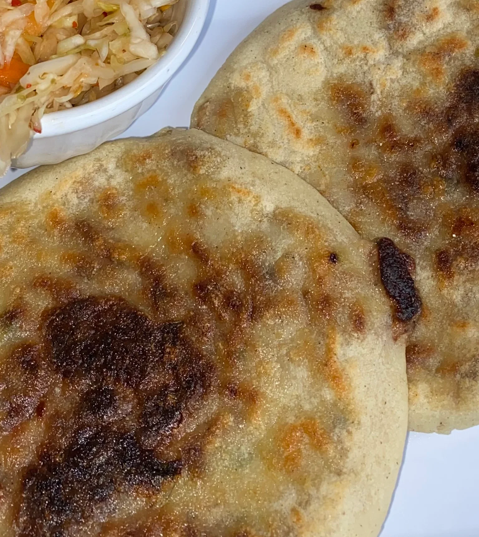 A plate of tacos filled with a variety of ingredients, topped with fresh chopped herbs and served with a small bowl of sauce.