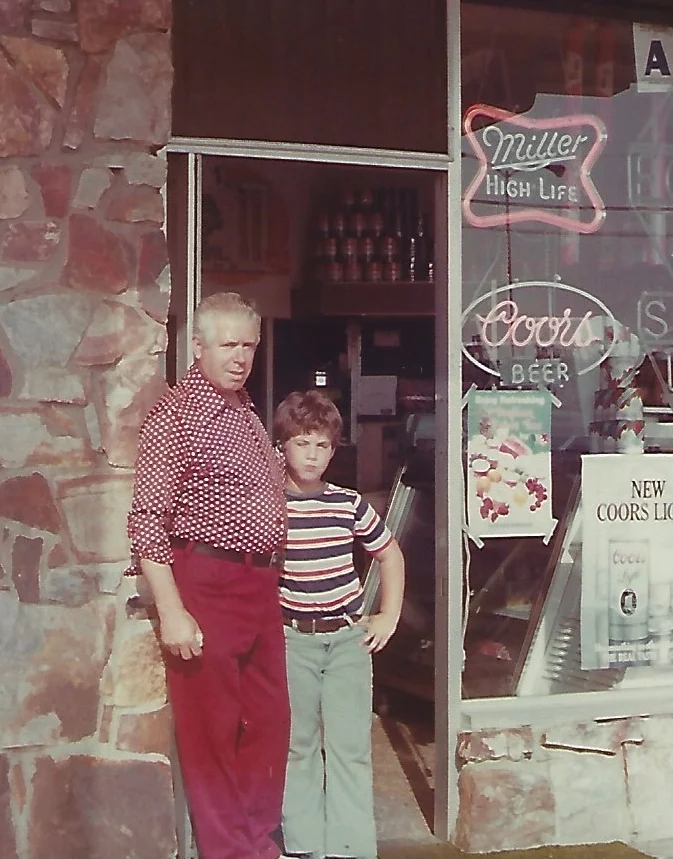 A man and a boy standing outside a store with neon signs.