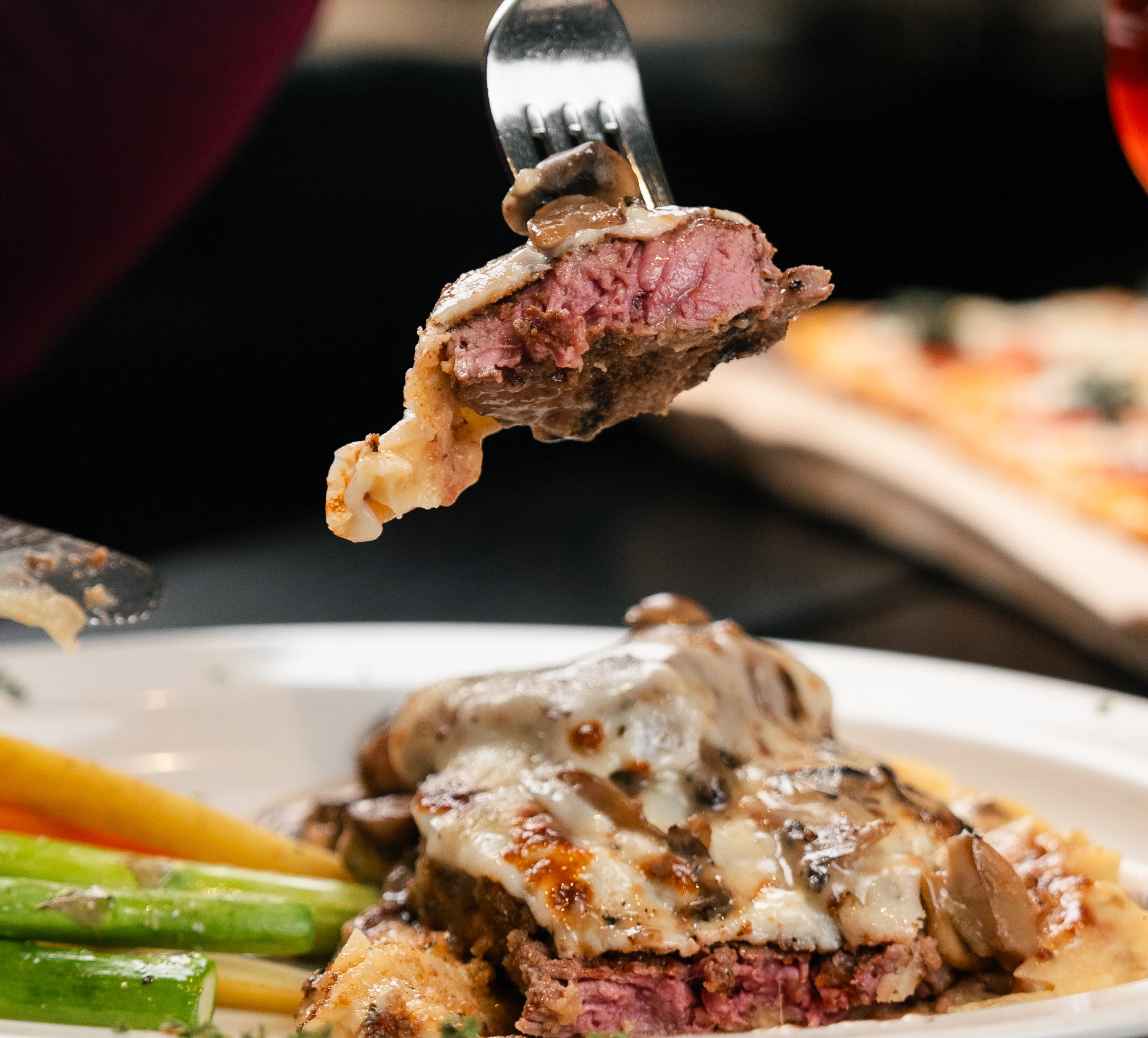 A fork holding a piece of medium-rare steak with vegetables on the side.