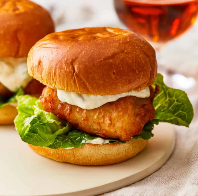 A delicious fish sandwich made with crispy fish fillet, fresh lettuce, and creamy sauce inside a soft bun.