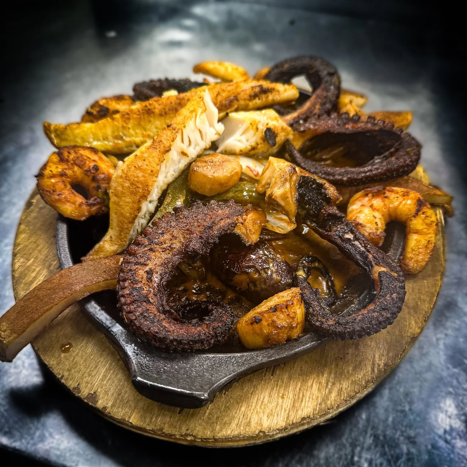 A sizzling platter of assorted grilled seafood, featuring shrimp, octopus, and fish, garnished with vegetables.