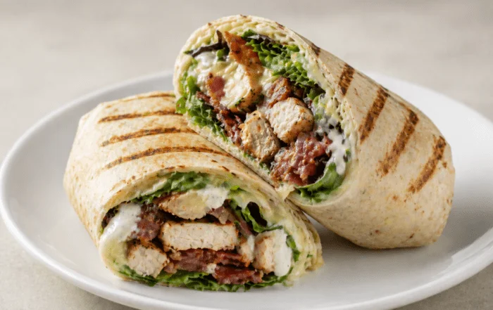 A grilled wrap stuffed with crispy chicken, lettuce, and creamy sauce, cut in half to display its delicious filling.