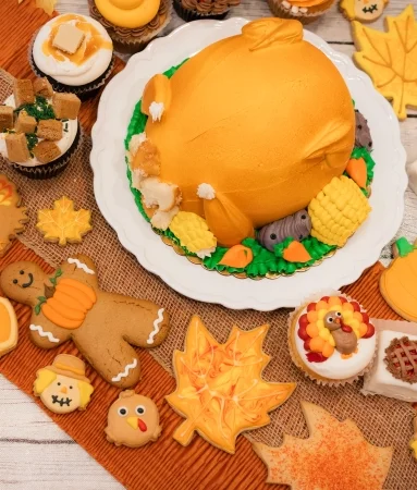 Pumpkin-shaped cake surrounded by autumn-themed decorated cookies